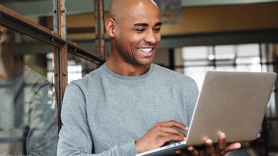 Happy man holding laptop while leaning against window