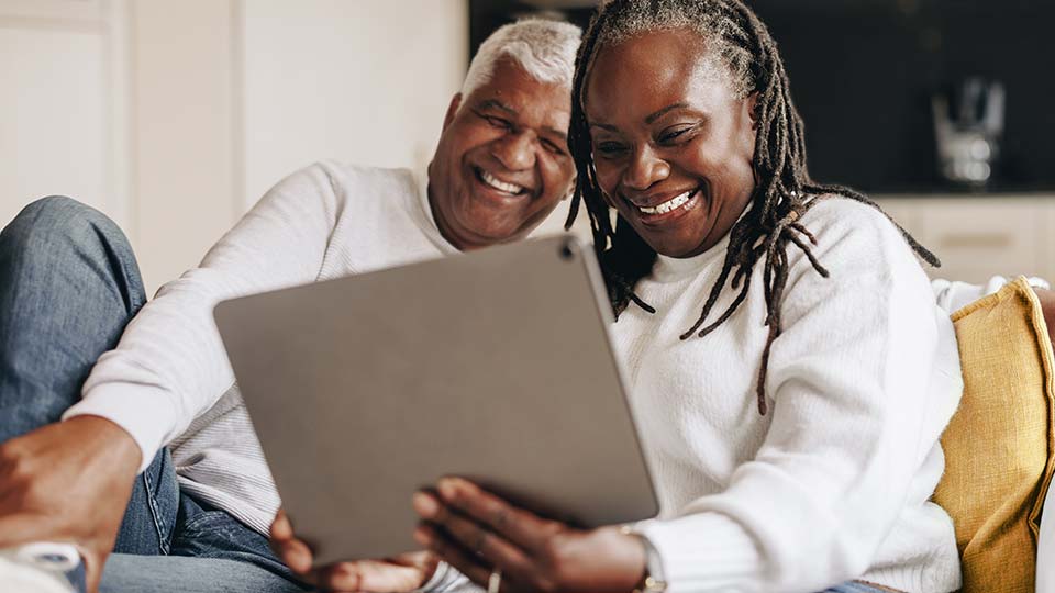 Mature couple happily using tablet at home