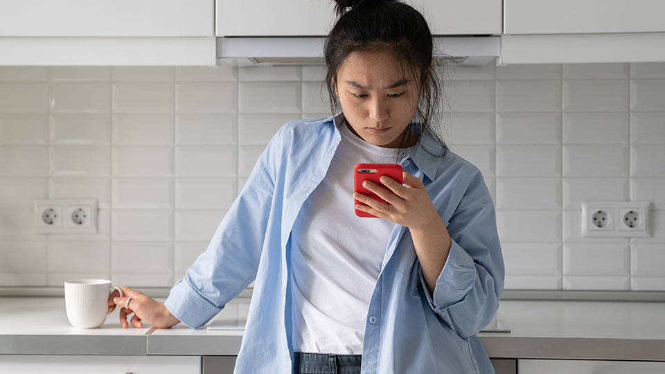 Upset young woman looking at her phone in the kitchen