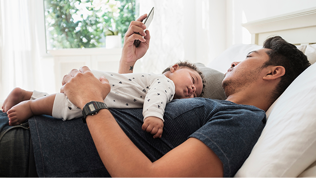Young father looking at phone with young baby resting in his arms