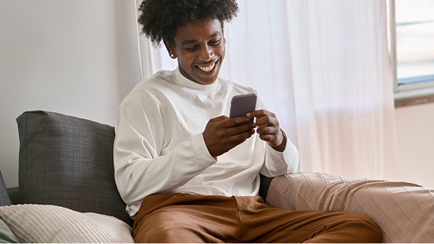 Man happily looking at his phone while on the couch at home