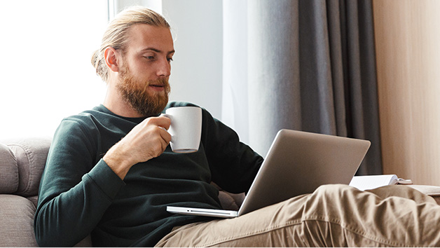 Man holding mug while looking at laptop