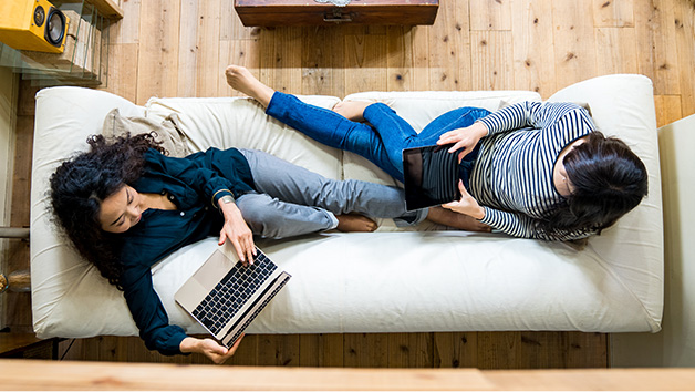 Two women using electronics while sitting on the couch