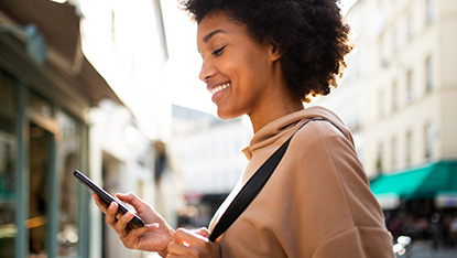 Young happy woman looking at phone in city