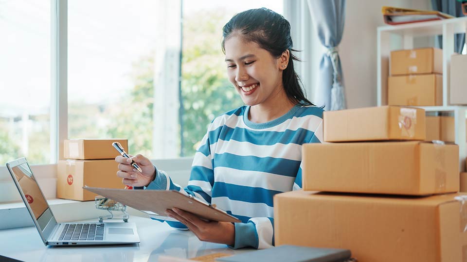 Happy Ecommerce merchant at desk with stacked boxes