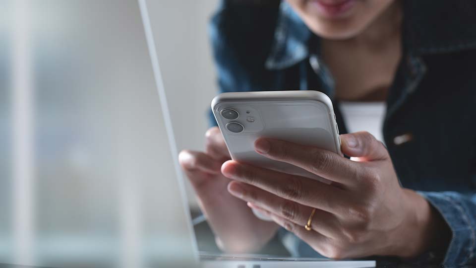 Close up shot of woman's hand tapping phone with laptop in view